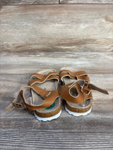 Rear view of Lucky Brand Kiara toddler sandals in brown showcasing cork footbed, adjustable buckles, and white ridged soles on wood background