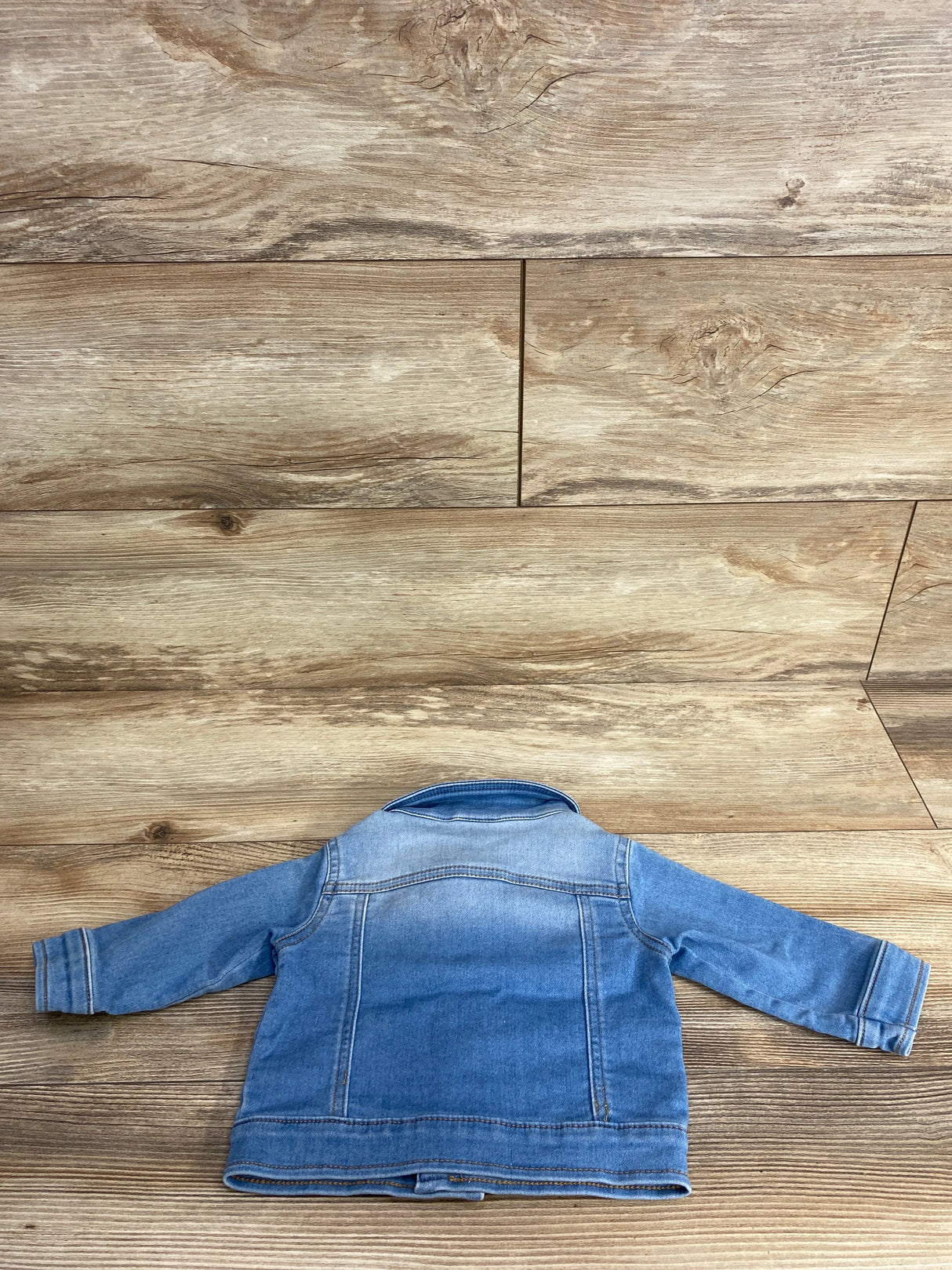 Back view of a blue denim jacket for kids laid flat on wood floor background, children's resale clothing