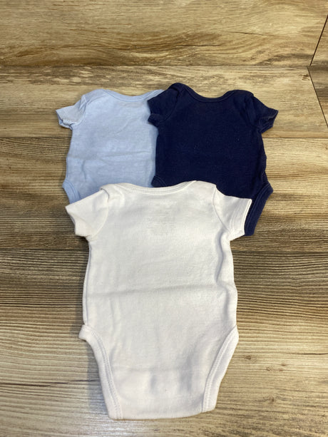 Three short-sleeve baby bodysuits in white, light blue, and navy on wooden floor