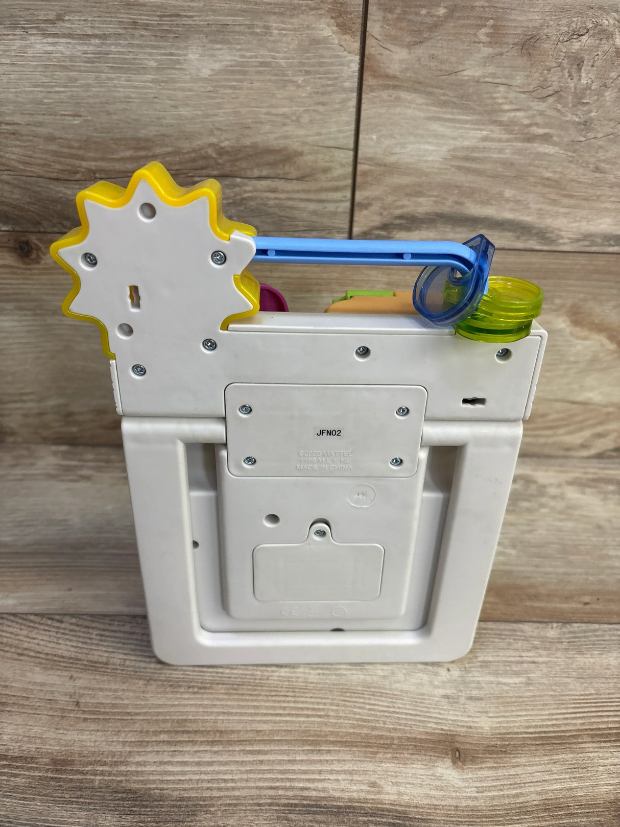 Rear view of Fisher-Price Peek & Play Busy Garden toy showing battery compartment and yellow gear with wood background