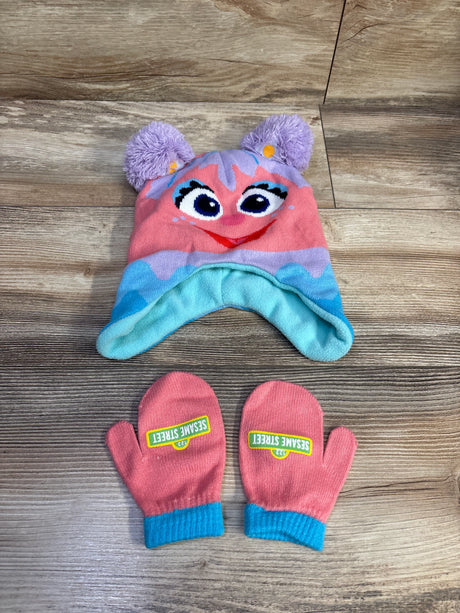 Top-down view of Abby Cadabby hat and mittens: pom-pom ear hat with embroidered face and coral mittens with turquoise trim