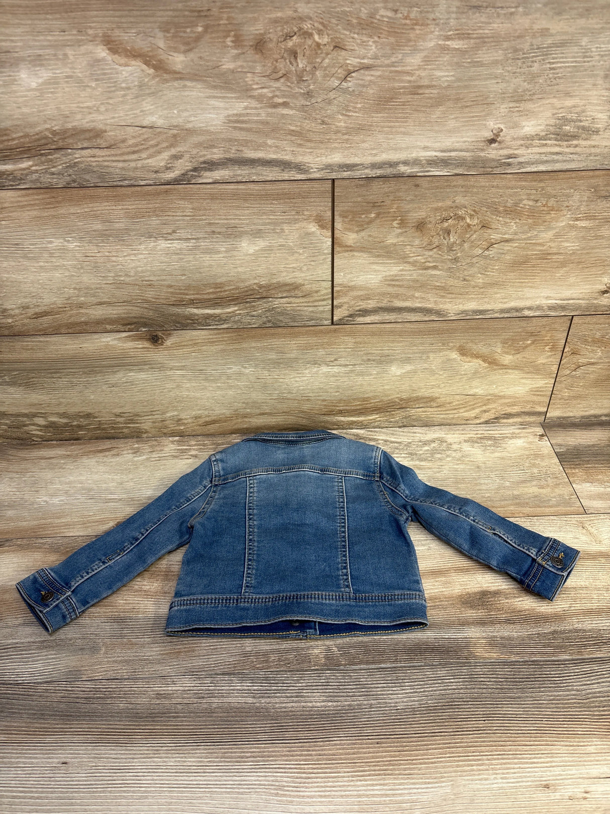 Back view of Cat and Jack denim jacket 18M showing stitched paneling, button cuffs and faded blue wash on wood background
