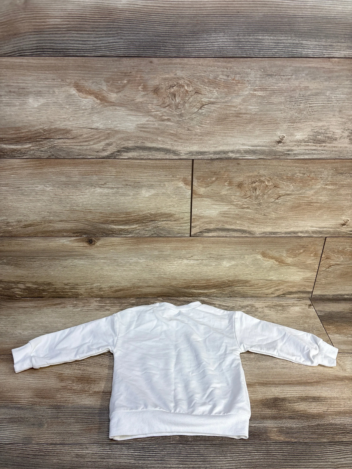 White long sleeve toddler sweatshirt displayed flat on wood background