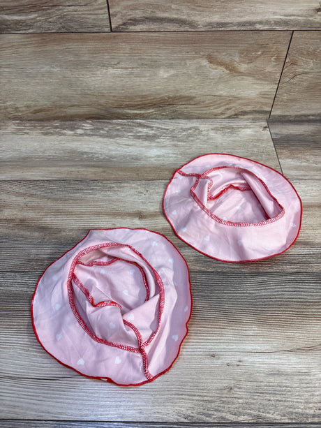 Top-down view of two heart-print baby bucket hats showing pink fabric with small white hearts and red edge trim on a wood floor