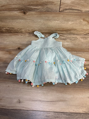 Light blue gingham baby dress with colorful pom-poms on wooden floor