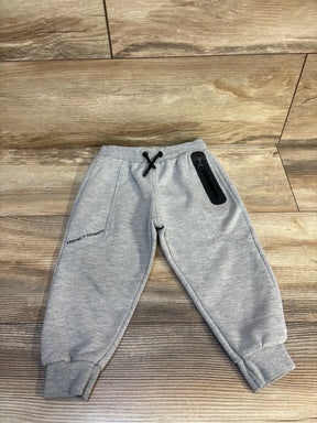 Gray kids joggers with 'Keeping It Authentic' text, black drawstring, and zip pocket on wood floor