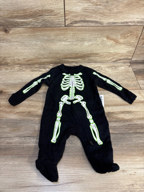Black baby skeleton onesie with glow-in-the-dark bones, Halloween costume for infants, laid on wood floor