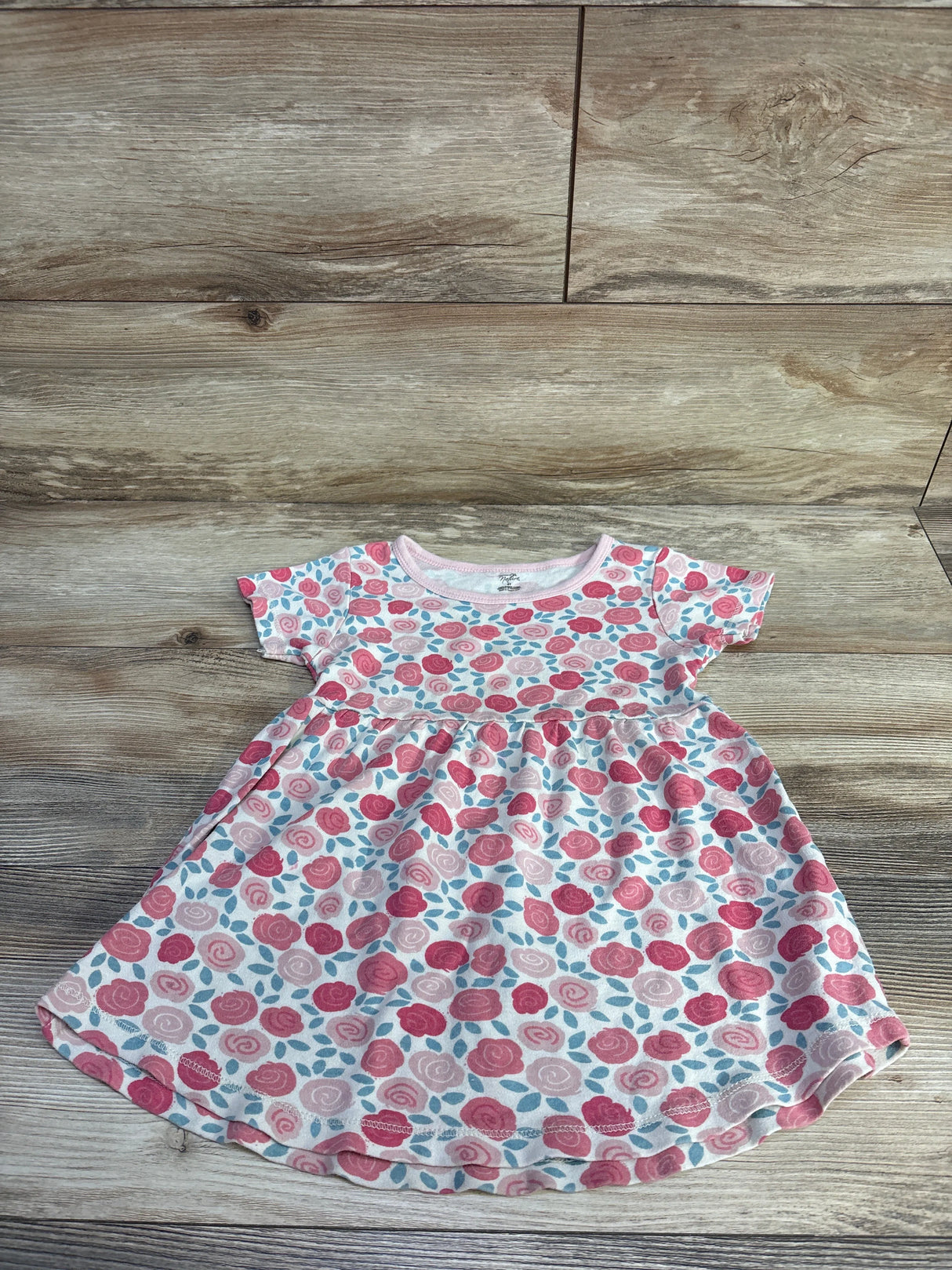 Flat lay of toddler floral dress by Touched By Nature showing pink rose print and gathered waist on wood plank background