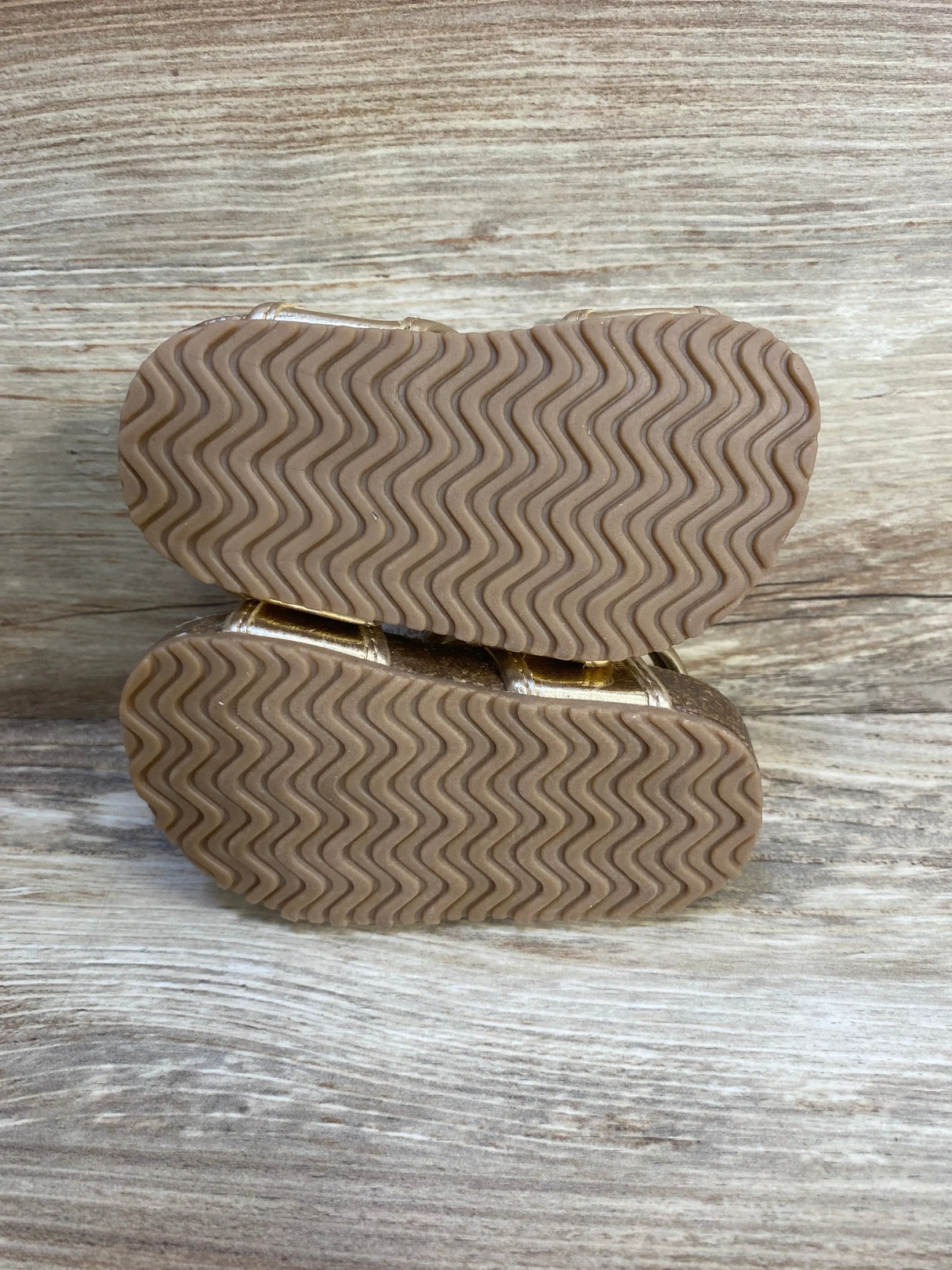 Bottom view of Just One You first-walker toddler sandals showcasing wavy rubber tread soles on wooden background
