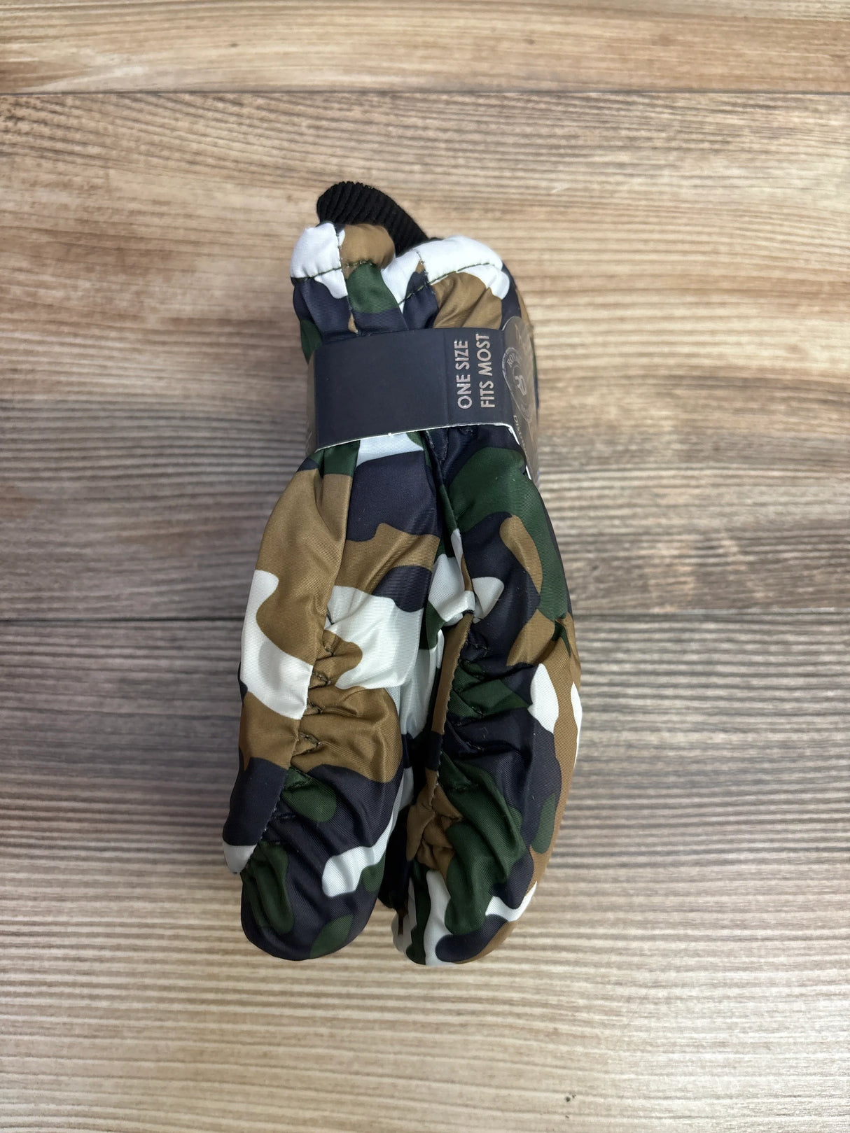 Pair of camouflage patterned winter mittens with elastic wrists on wooden surface