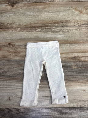 White baby leggings with subtle pink polka dots and a small logo on the ankle, laid flat on wood