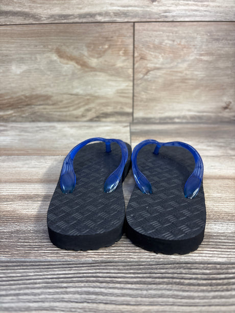 Front view of Locals Original toddler flip flops size 7.5C showcasing translucent blue straps and textured black soles on a wood-look floor