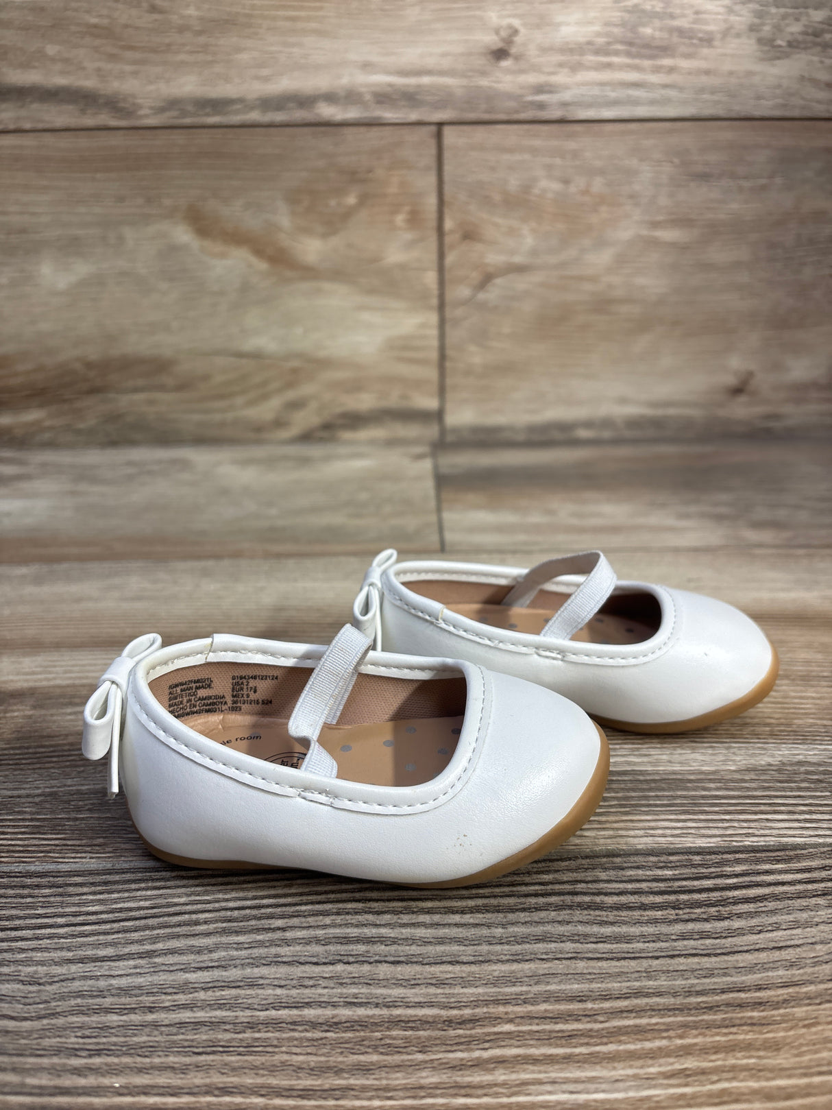 Side view of Wonder Nation white toddler ballet flats with elastic strap and back bow, gum sole on wood floor