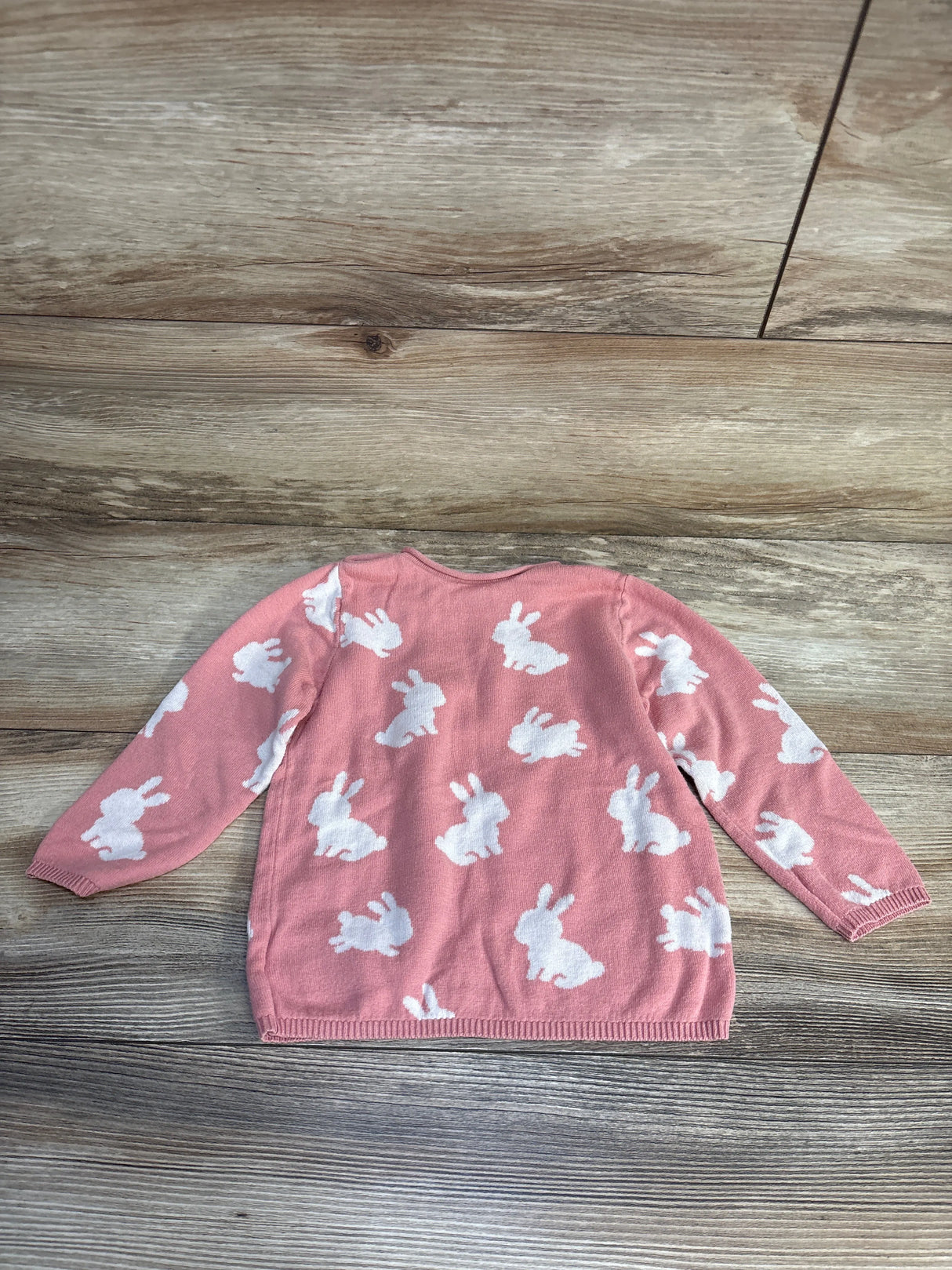 Pink kids sweater with white bunny print, long sleeves, laid on wood floor