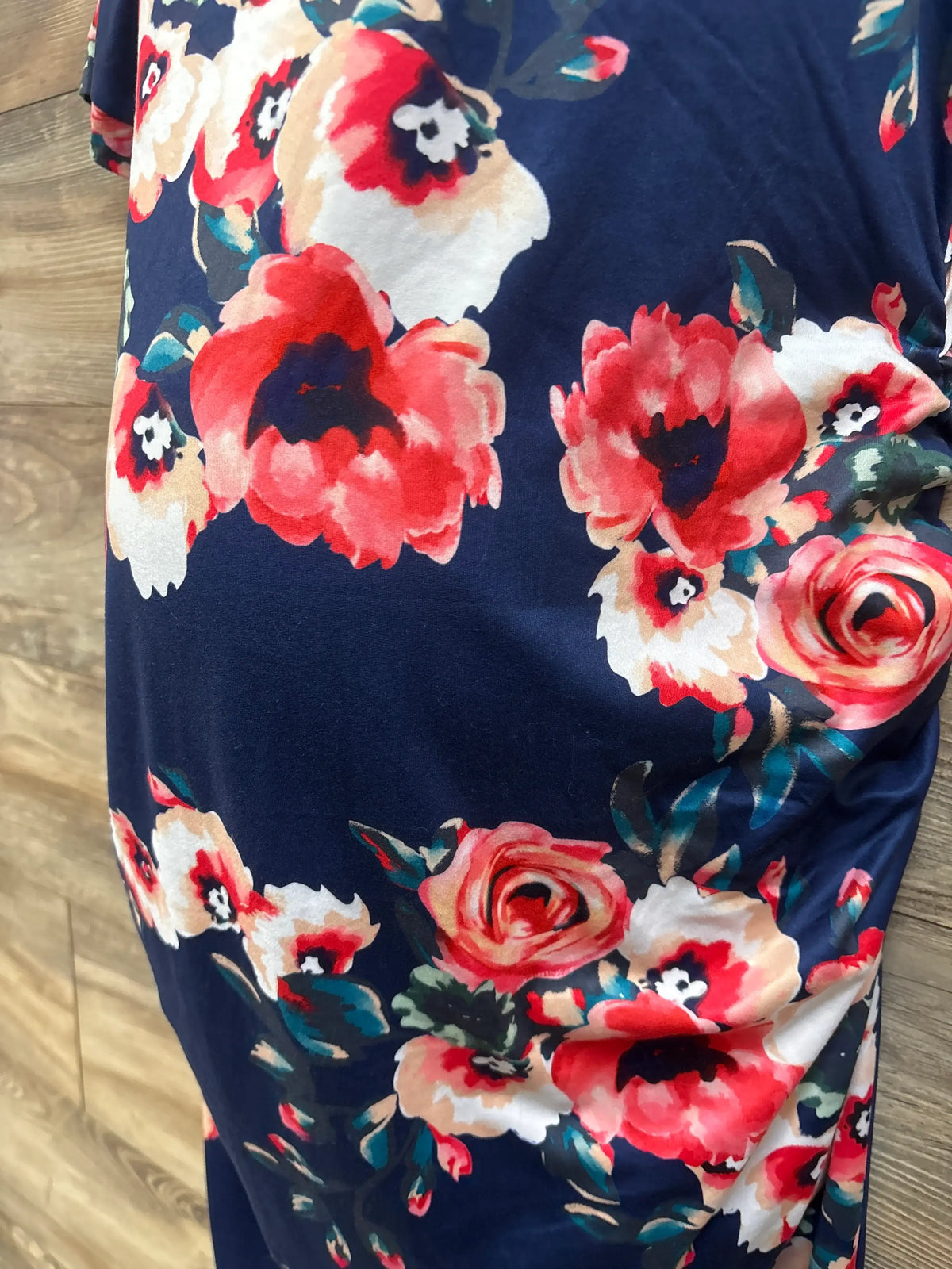 Close-up of Musidora floral maternity ruched dress in navy showcasing its multicolor floral print with a wood floor background
