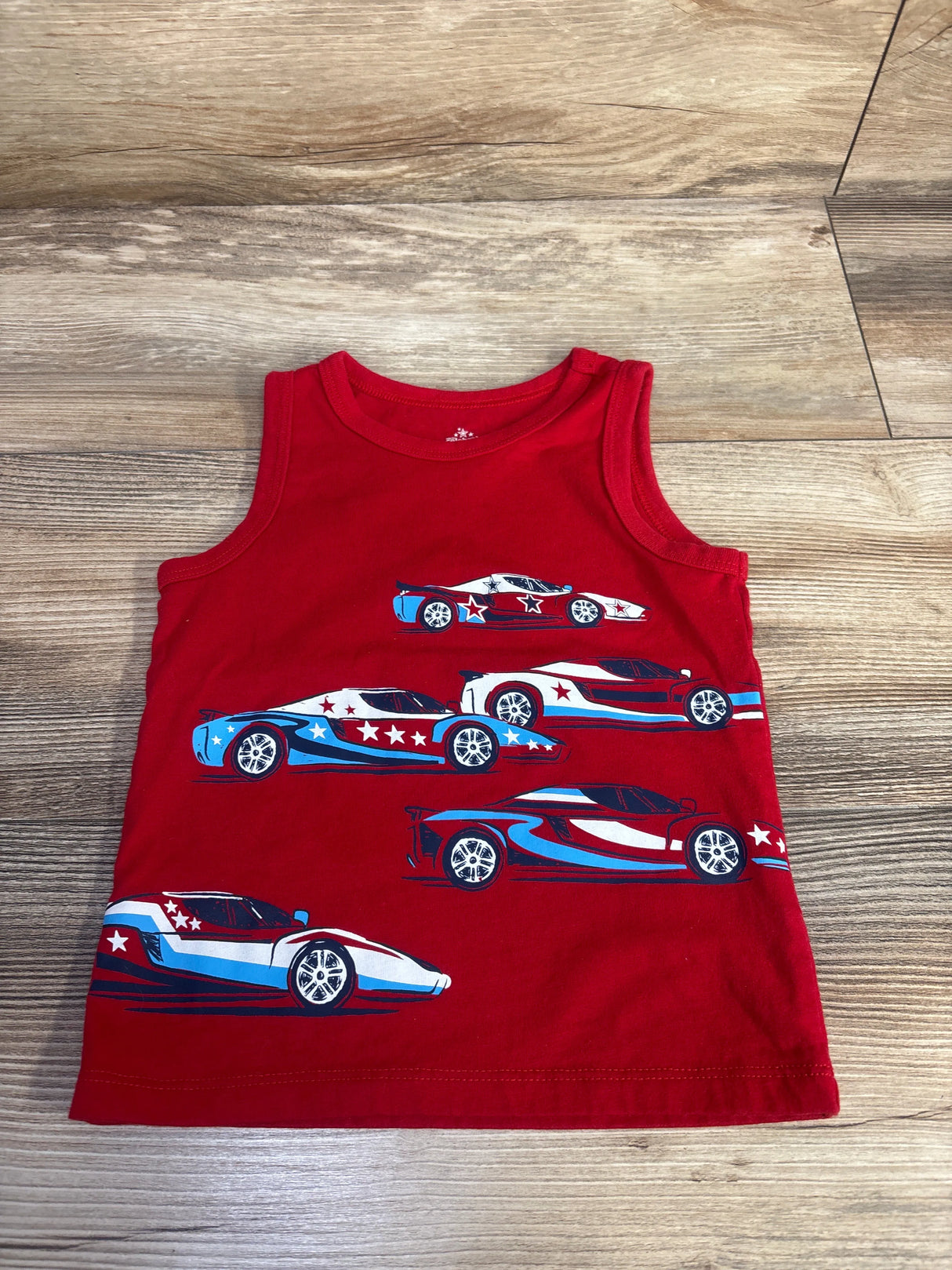 Flat lay of red toddler tank top showcasing blue-and-white patriotic racing car and star prints on wood floor