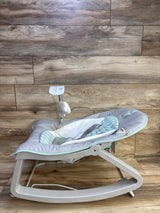 Side view of Ingenuity Keep Cozy 3-in-1 bouncer showing padded grey and mint seat, toy bar, and plastic rocker on wood floor
