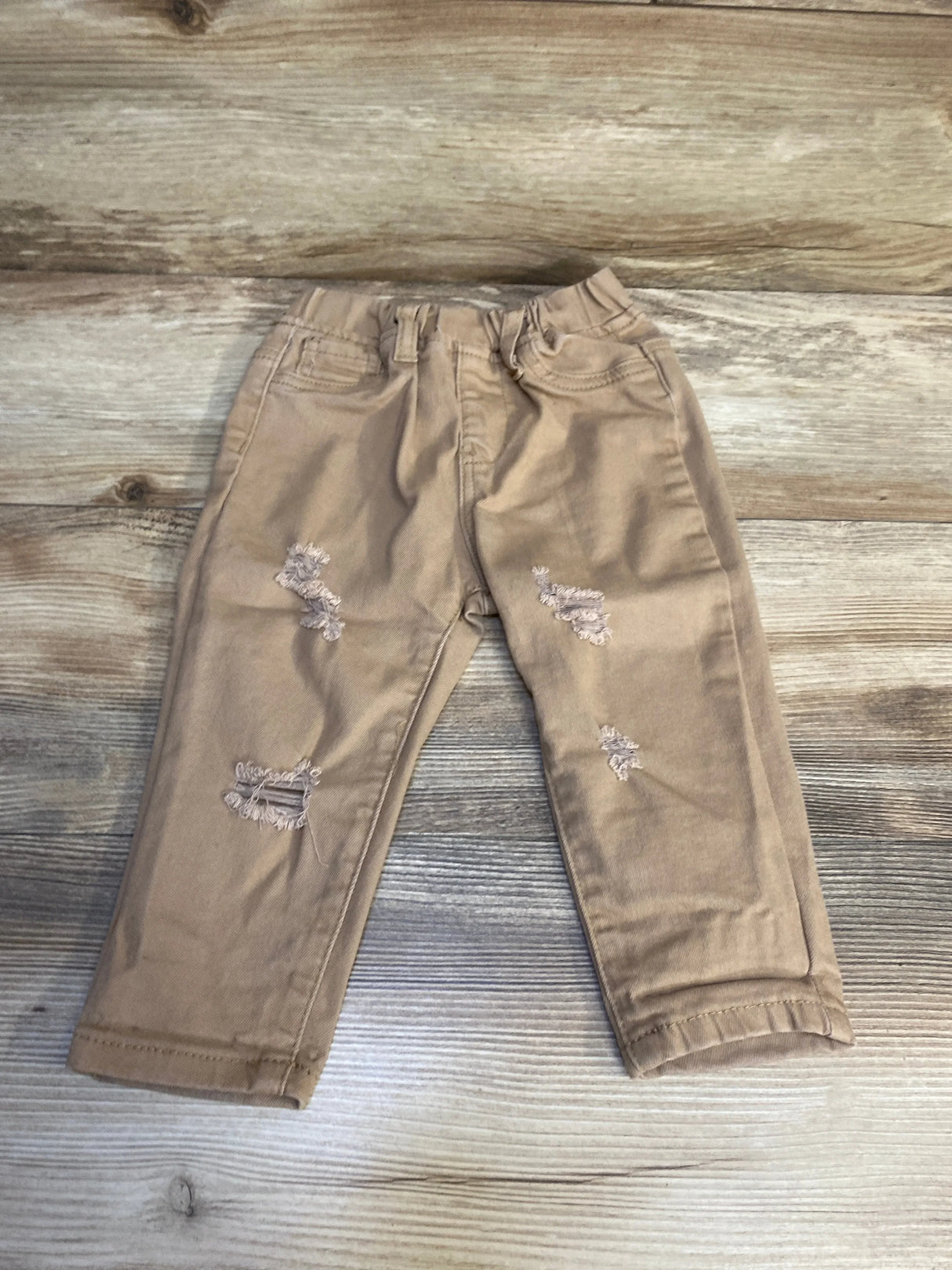 Tan distressed toddler jeans with front pockets on wood background