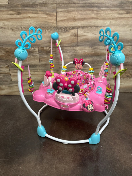 Front view of Disney Baby Minnie Mouse PeekABoo Activity Jumper with pink seat, hanging toys, and turquoise arches