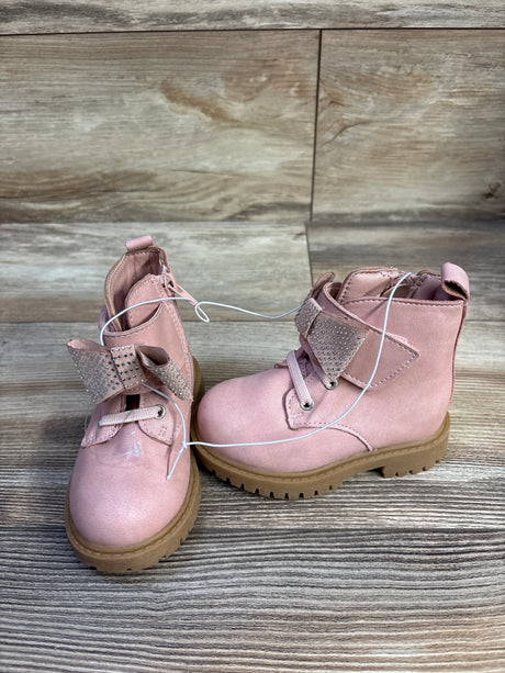 Front three-quarter view of Jessica Simpson Daria pink toddler ankle boots showcasing rhinestone bow strap and tan lug sole on wood background