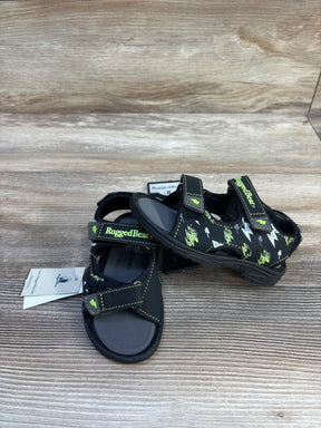 Front three-quarter of Rugged Bear kids' black sandals with green lightning print and Velcro straps on wood background