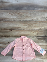 Light pink long sleeve kids button-up shirt with tag on wood background