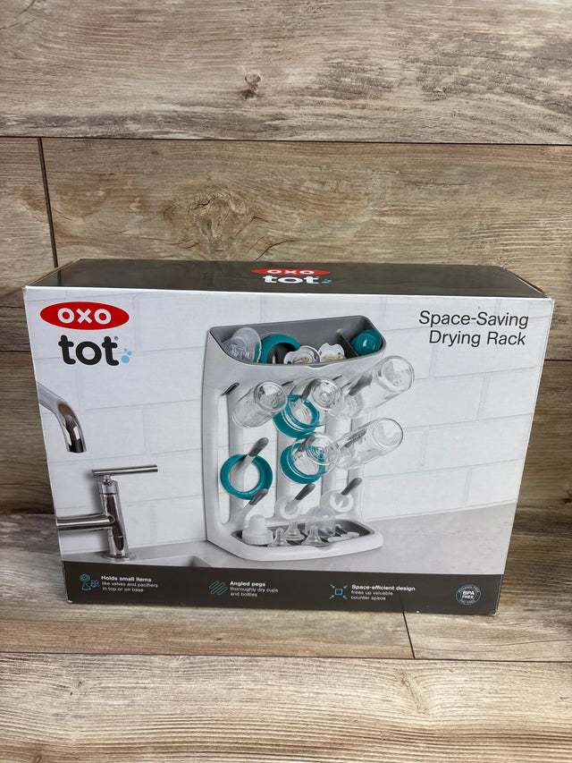 Front view of OXO Tot Space Saving Drying Rack box showcasing angled pegs and space efficient design on a wood floor