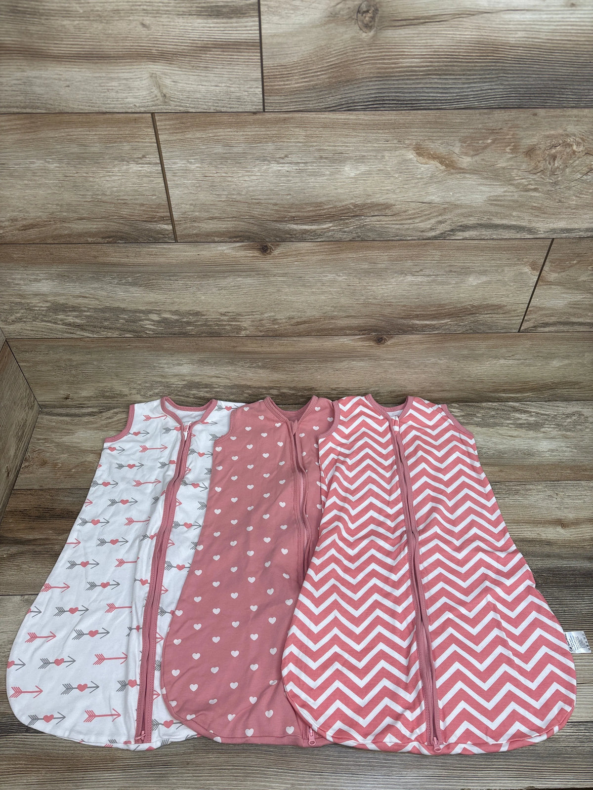 Top view of Yoofoss sleep sacks in white and pink with arrow, heart, and chevron patterns on a wood floor