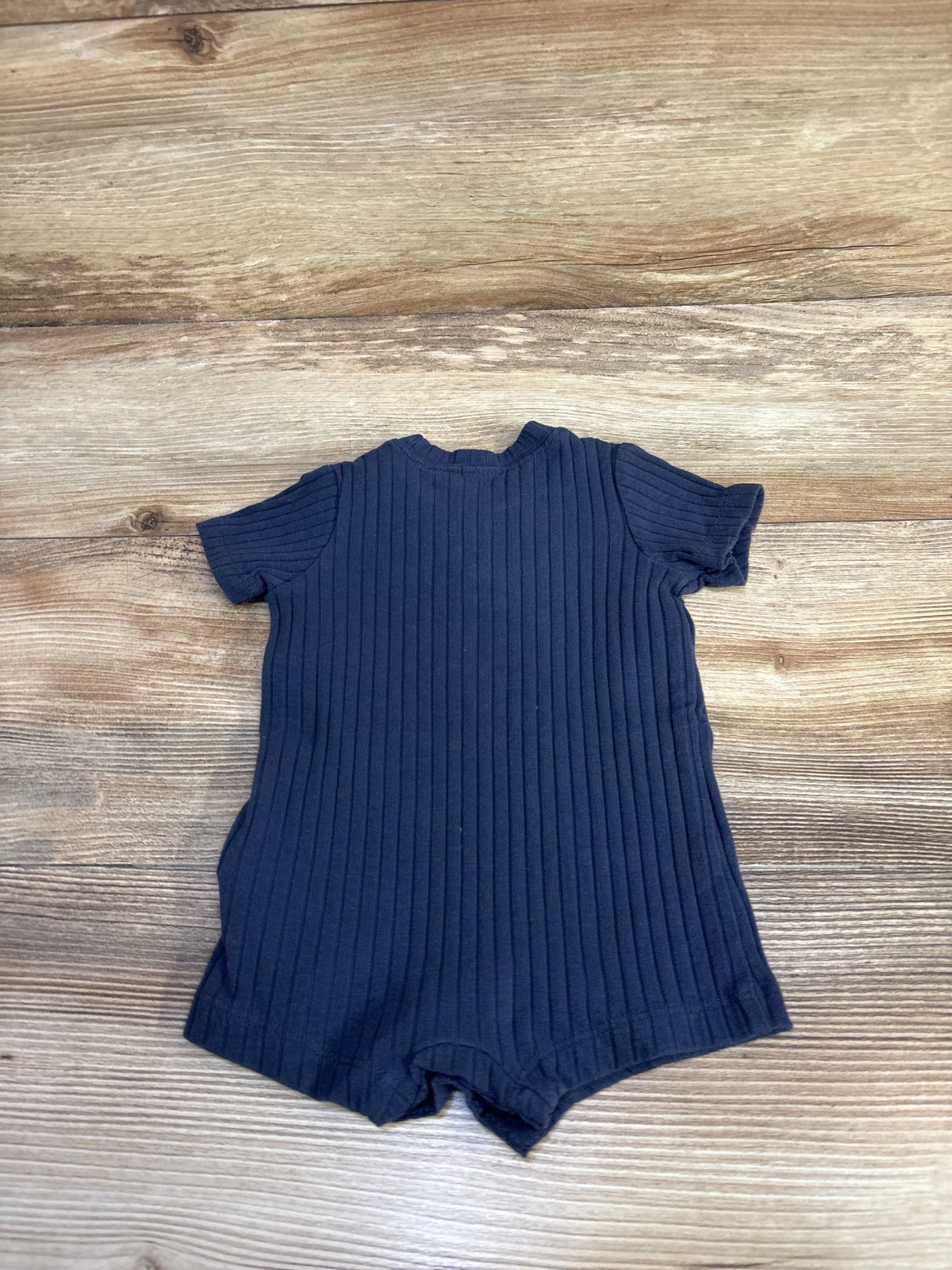 Flat-lay of navy ribbed baby shortie romper showing short sleeves and vertical ribbing on wood background