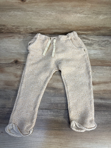 Beige knit baby pants with drawstring waist and rolled cuffs on wooden background