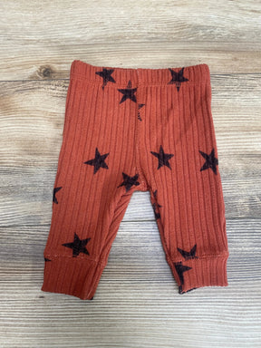 Flat lay of Grayson Collective ribbed newborn pants in rust with black stars, elastic waist and cuffed ankles on light wood