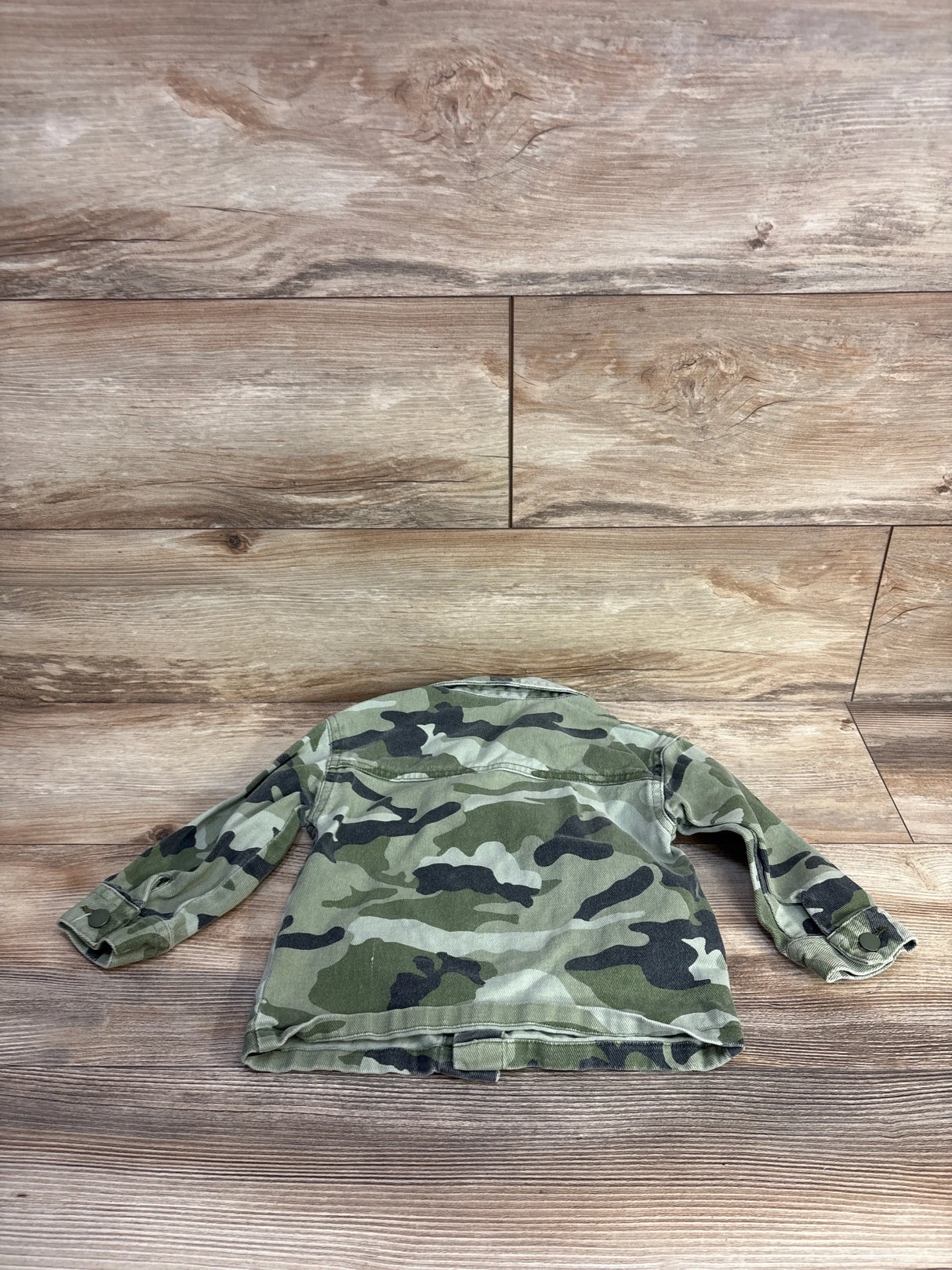 Back view of toddler camo denim jacket size 2T showing green camouflage print, long sleeves and button cuffs on wood plank background