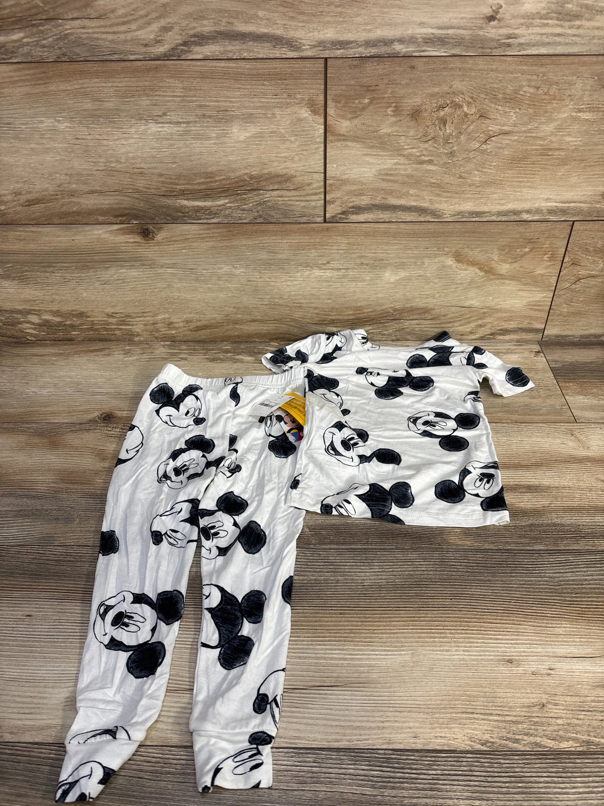 Flat lay of white Disney Mickey 2-piece short-sleeve viscose pajama set size 3T with black Mickey face print on wood floor