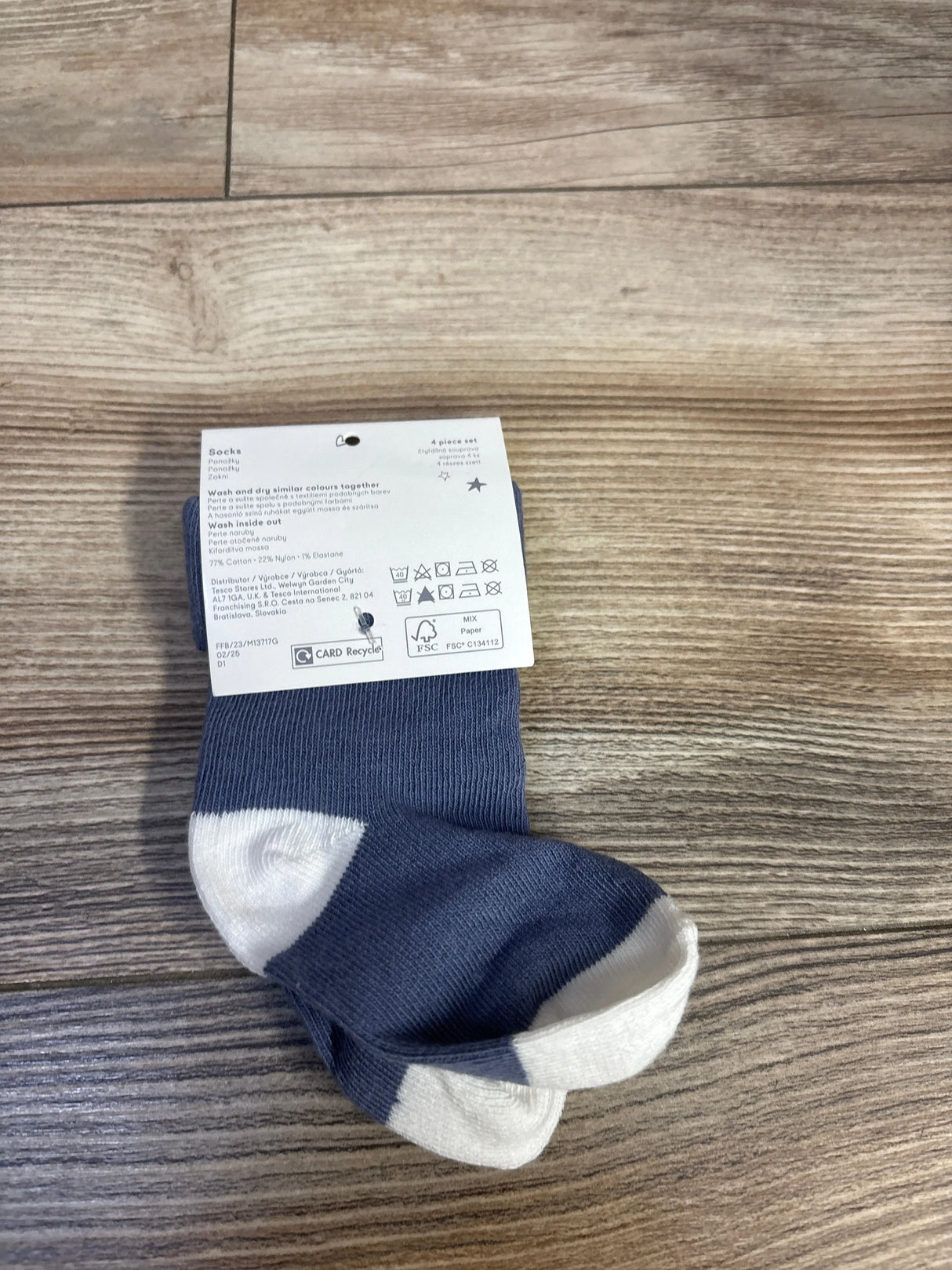 Top-down view of Fred & Flo blue baby socks with white heels and toes, folded with product tag on wood floor