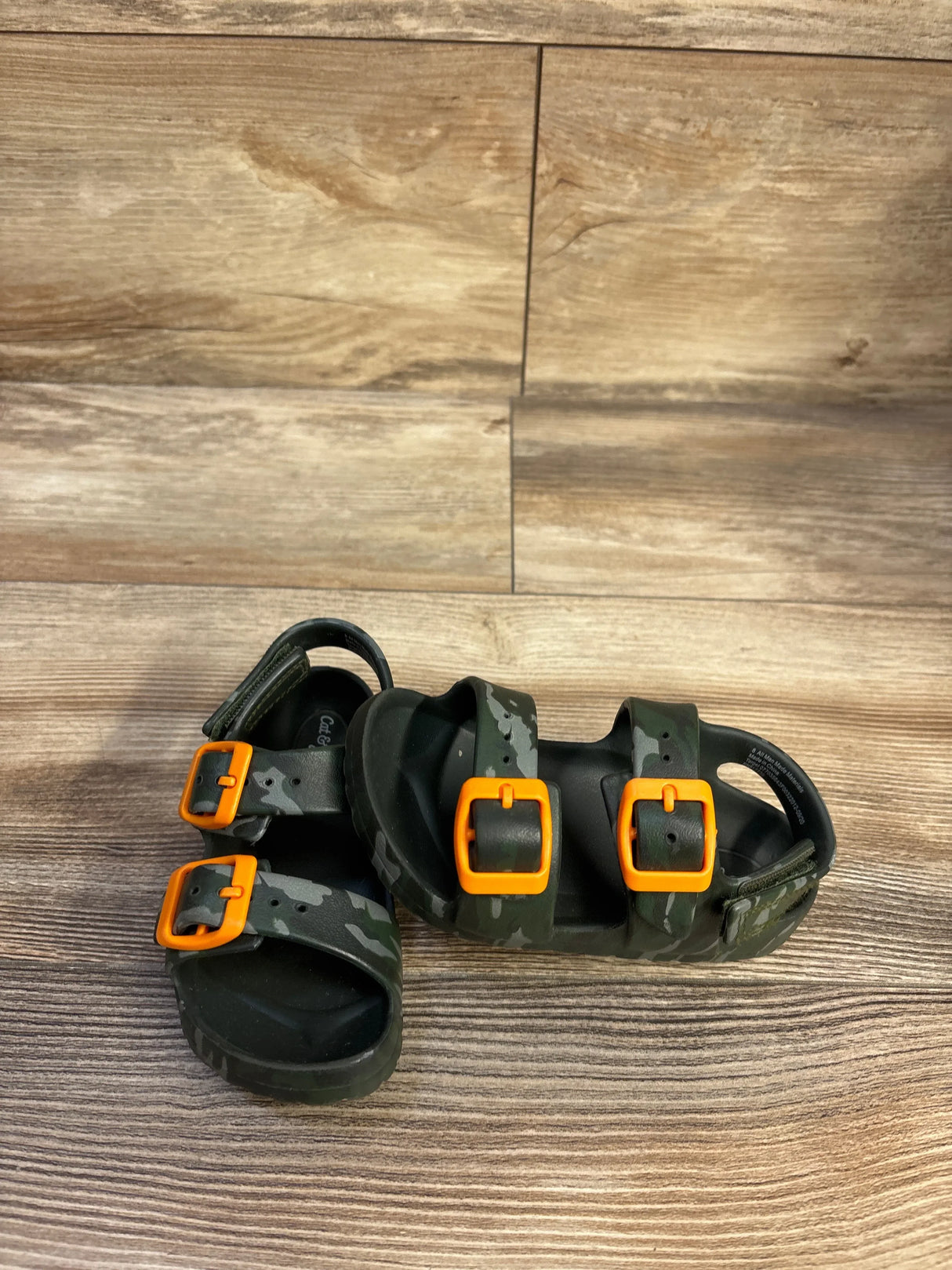 Angled overhead view of Cat and Jack Ade footbed sandals with camo print and orange buckles on wood floor