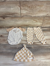 Flat lay of beige ribbed 3-piece set: bodysuit, checkered pants, and knotted hat with ribbed texture and snaps on wood floor
