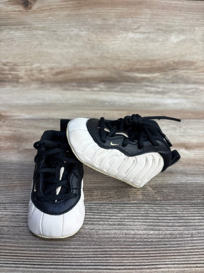 Three-quarter view of Nike Posite One crib booties showing black-and-white molded foamposite-style upper and lace closure on wood background