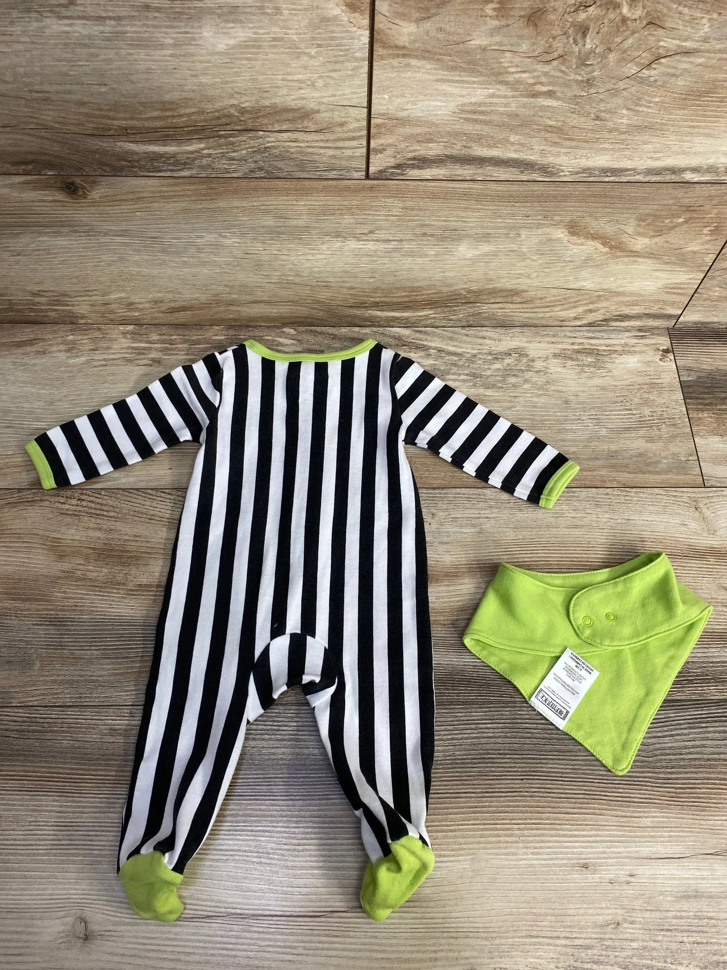 Black and white striped baby onesie with lime green accents and matching bib on wood floor