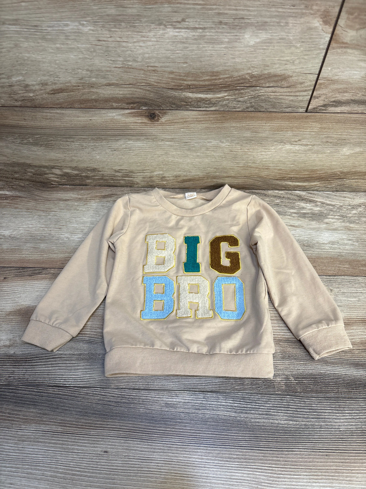 Beige toddler sweatshirt with colorful BIG BRO letters on wood background, kids clothing