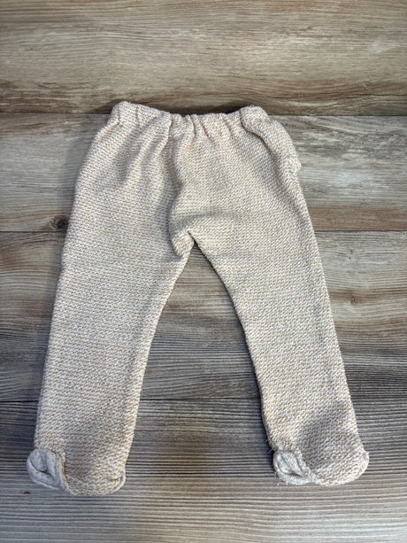 Beige knit baby pants with footies, elastic waist, laid flat on wood background