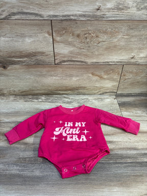 Flat-lay front view of hot pink long-sleeve newborn bodysuit showcasing IN MY MINI ERA print and snap closures on light wood background