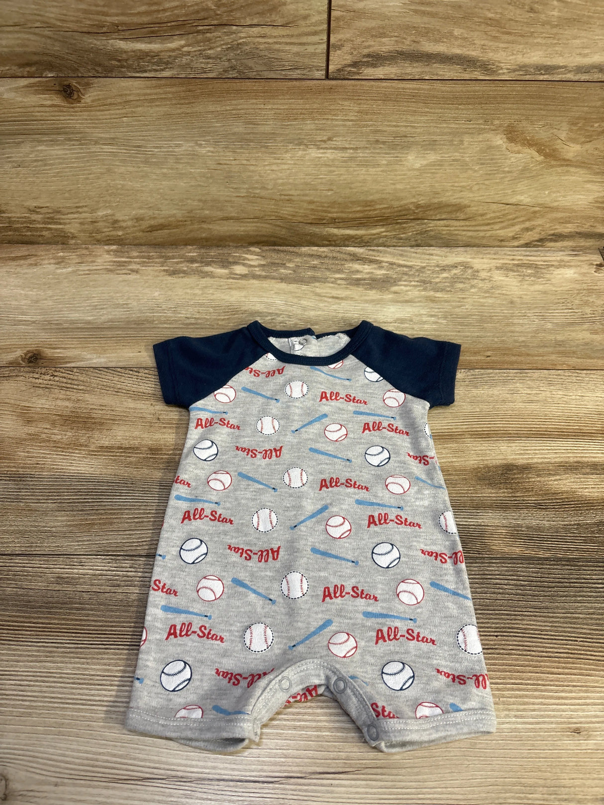 Front view of Little Beginnings All Star Shortie Romper, grey size 0-3m, with baseball print and navy sleeves on wood floor