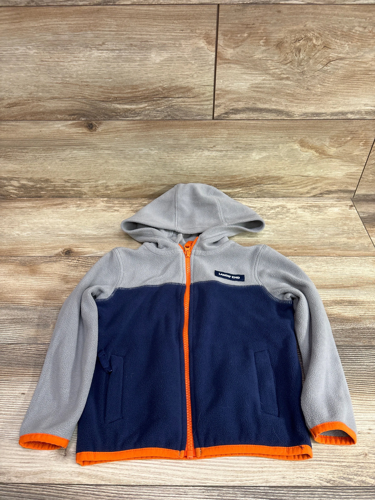 Front view of Lands End full zip fleece jacket showcasing gray and navy color blocking, hood and orange zipper on wood flooring