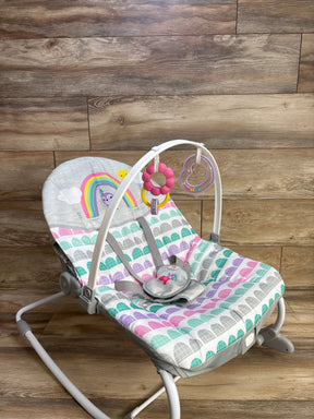 Angled front view of Bright Starts Rosy Rainbow rocker with pastel scallop seat, toy bar with pink flower and purple heart