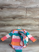 Flat lay of Eddie Bauer long-sleeve one-piece swimsuit and hat, multicolor stripes and ruffle trim on wood background