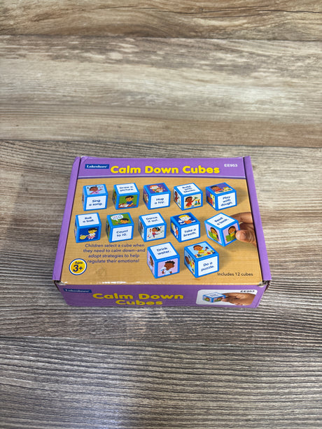 Top view of Lakeshore Calm Down Cubes box showcasing illustrated activity cubes and a hand holding a cube on a wood tabletop