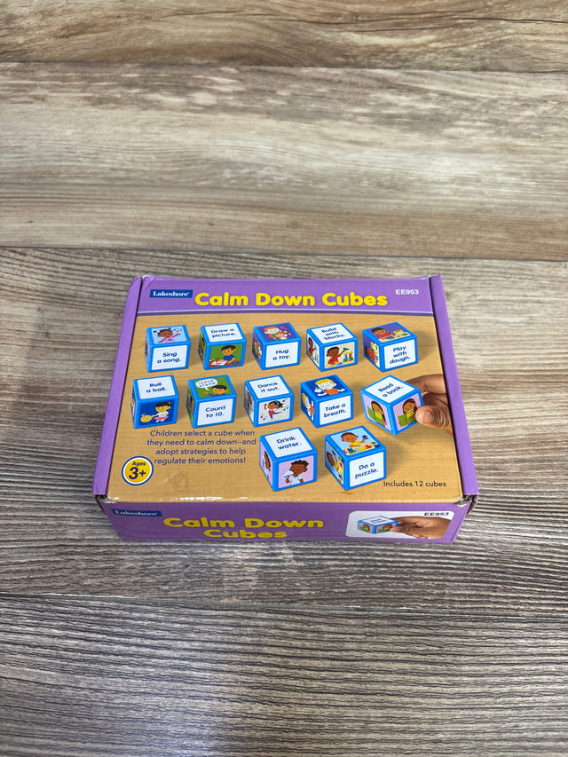 Top view of Lakeshore Calm Down Cubes box showcasing illustrated activity cubes and a hand holding a cube on a wood tabletop