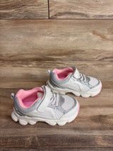 Angled view of Carter's white athletic sneakers showcasing silver glitter and pink lining with wood floor background