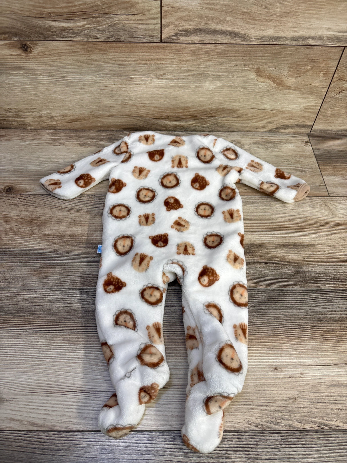 Front view of Little and Loved plush footed blanket sleeper, white fleece with brown lion-face print on wood floor