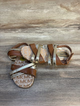 Brown and gold toddler sandals with MK logo, strappy design on wood background